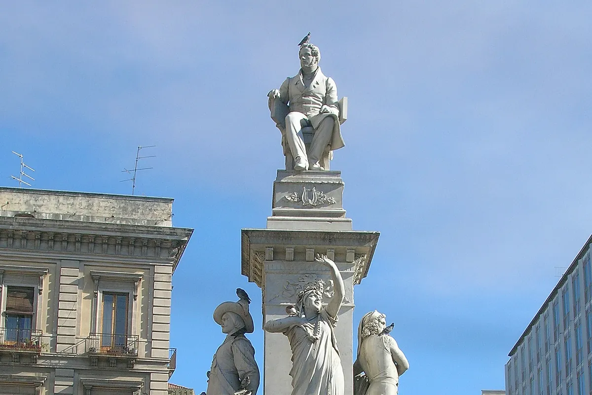 The Bellini monument in Piazza Stesicoro in Catania, a white marble figure of the composer seated on a tall plinth with statues around its base under a blue sky